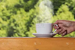 在森林的背景下，在木甲板上，一个女人的手拿着一杯热饮，蒸汽从杯子上升起。早上好概念