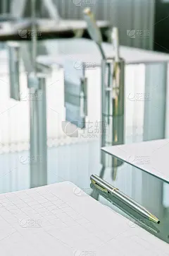 等待会议。水晶桌子上配有便签纸、笔和名片，反射着窗帘的垂直条纹，这些条纹切断了大窗户的光线