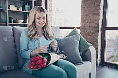 她的肖像，她漂亮迷人，漂亮开朗，愉快的波浪形头发的女孩坐在沙发上阅读贺卡，问候生日庆典在现代工业阁楼