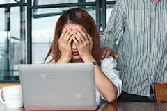 手的同事安慰沮丧悲伤的亚洲妇女手捂脸在办公室的工作场所哭泣。