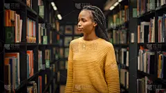大学图书馆：在各排书架之间寻找合适的课题名称的精美黑人女生肖像