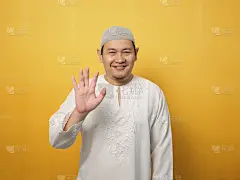 穆斯林男子戴着头巾看着镜头微笑，在黄色背景下挥手问好或告别