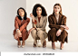 interracial young women in trendy suits sitting and posing on white Stock Photo