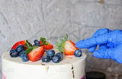 糕点师女孩戴着手套用新鲜的草莓和蓝莓装饰蛋糕