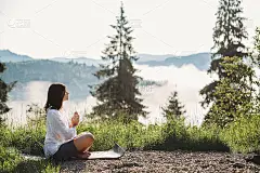 在阳光明媚的晨光中，一名年轻女子在山顶的草丛中练习瑜伽，坐着莲花体位。冥想。平静宁静的时刻，与大自然