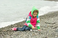 一个七岁小女孩坐在卵石滩上