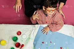 特殊教育的老师和学生穿着长袍，在桌子上用手画着生日花环和涂着丙烯颜料的黄色纸板。塑料工艺疗法。