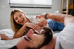 英俊的年轻夫妇花时间一起在家里的床上说说笑笑
