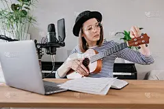 播客，音乐音频内容的创作。美丽的欧洲女性播客主播戴着一顶帽子，拿着一把吉他或尤克里里琴，电台主持人在