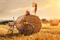 Fashion photo, beautiful woman sitting on a bale of wheat, next to the old bike by Gergely Zsolnai