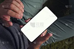 一个年轻人使用白色屏幕的智能手机的倾斜的自上而下的视图。男子右手拿着智能手机，准备用左手触摸屏幕。人
