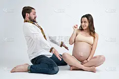 年轻的胡子男子在白色衬衫的震惊，把他的胳膊分开，坐在他美丽的怀孕的睁大眼睛的妻子在米色胸罩，孤立在白