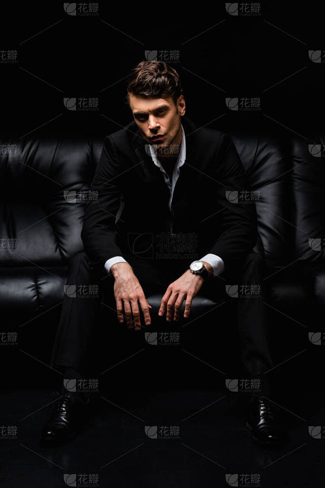 正装男子坐在黑色背景的沙发上 