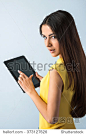 Photo of beautiful young business woman standing near gray background. Woman with yellow shirt using tablet computer and looking at camera