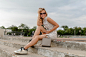 Free photo young attractive stylish blonde woman sitting in city street in summer fashion style dress wearing sunglasses, purse, silvers sneakers