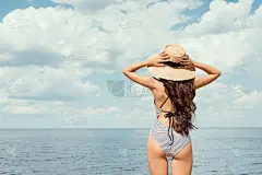 背影的女孩在游泳衣和草帽看海