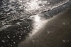 一个带着金色沙子的泡沫的波浪来到了海岸。晚上海上冲浪。阳光照在水面上。日落时分，河堤风平浪静