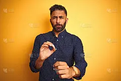 年轻英俊的印度商人穿着衬衫，上面孤立的黄色背景令人厌恶的表情，不高兴和恐惧做厌恶的脸，因为厌恶的反应