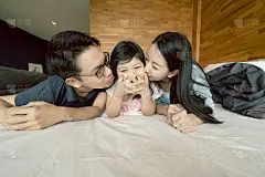 幸福快乐的亚洲家庭的妈妈，爸爸，女儿躺在一起，与有趣的玩亲吻在床上的亚洲家庭的人的家庭背景