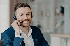 快乐的年轻商人戴着耳机和麦克风在室内与客户交谈