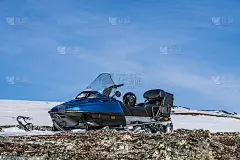 一辆蓝色的雪上摩托高高地站在挪威山上的雪和石头上，温暖的日子和非常明亮的太阳，没有云，雪开始气味，挪