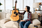 Cute woman with guitar at home, headphones. pretty lady with musical instrument relax in the room, female music lover resting
