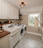 Inspiration for a country single-wall ceramic tile and gray floor dedicated laundry room remodel in Philadelphia with a farmhouse sink, white cabinets, wood countertops, a side-by-side washer/dryer and brown countertops