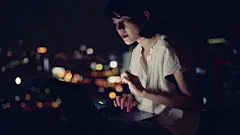 年轻的亚洲女人坐在阳台上用笔记本电脑工作