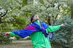 年轻英俊的白人男子与明亮的怪胎运动装70年代风格站在一个早晨的公园。