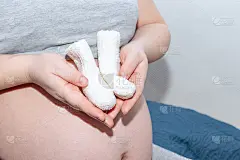 快乐的母亲的概念。女人的手拿着编织的袜子在一个孕妇的肚子的背景