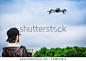 Closeup of Young boy wearing black hat playing with a black drone and control it by using mobile phone connection, against blue sky