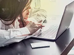 美丽的亚洲商务女性(30 - 40岁)，白色的衬衫使用电脑笔记本电脑，把名片盒放在桌子上，以支持她的