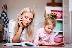 年轻的妈妈在家躺在地板上看书陪女儿在家，孩子在平板上看动画片玩，幸福的家庭，爱的家庭理念。