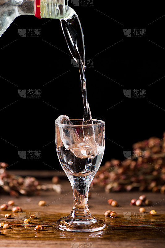 在木头背景上，中国白酒从瓶子里倒进玻璃杯...