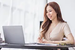 点击来源直接获取大图文件 |年轻的亚洲女商人在现代办公室使用笔记本电脑开心工作的肖像，自由职业商务员工在线营销电子商务电话营销概念。