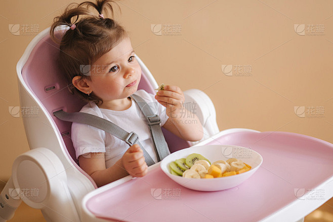 快乐的小女婴在高椅子上吃异国水果的肖像