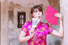 喜气洋洋的年轻女子穿着粉红色旗袍手持吹风，红包里装着吉祥如意的钱，家人给她看东西。庆祝中国新年的概念