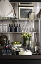 Modern and clean open-shelf kitchen storage housing Ralph Lauren Home essentials: Sackett barware and Asher porcelain serving pieces with black leather handles.