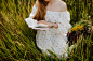 a woman sitting in a field of tall grass reading a book