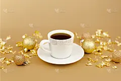 咖啡杯与茶碟，金色的圣诞球和金纸爆竹在金色的背景。香气和元旦早上好概念。前视图,特写镜头。