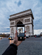 The hand of a man taking a photo of the Arc de Triomphe with his iPhone mobile smartphone while in traffic.