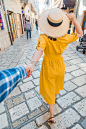 跟我来的概念。身穿黄色背心、头戴草帽的女子牵着男子的手走在小度假城市街道前
