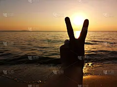 夕阳西下时，海滩上男子手握v字手势的剪影。明天的更新。目标和希望的概念。