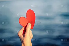 情人节概念，柔焦点女人手捧红心，模糊大海背景。卡片与一个男人的手雕刻红纸心在一个美丽的蓝色海洋的背景