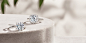 David Yurman DY Crossover® and DY Capri® engagement rings in platinum with diamonds on a beige stone surface with green leaves in the background.