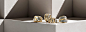 A color photograph shows four David Yurman rings from the Bold Renaissance, Crossover, Helena and DY Origami collections atop a beige-hued stone shelf with hard diagonal shadows. The women’s rings are crafted from sterling silver with 18K yellow gold deta