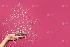 圣诞树上的五彩纸屑落在女人的手上，映衬着鲜艳的粉红色横幅背景