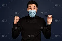 被治愈的冠状病毒的快乐男子，穿着黑色毛衣，戴着无菌面罩，拿着温度计，隔离在太平洋蓝背景下的演播室。冠