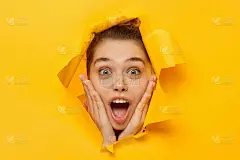 特写的年轻兴奋的女人震惊和惊讶的商业报价，透过破纸的洞，孤立在黄色的背景