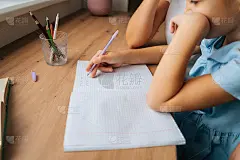 特写镜头:小女儿拿着笔在字帖上写作业，年轻的妈妈坐在靠窗的餐桌旁。